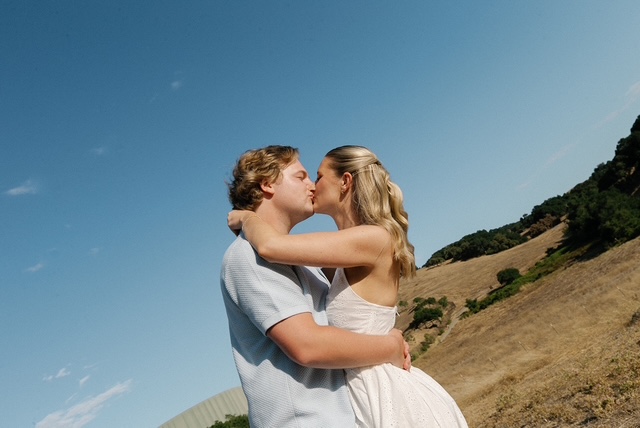 Chloe and Cal kissing on a sunny hillside