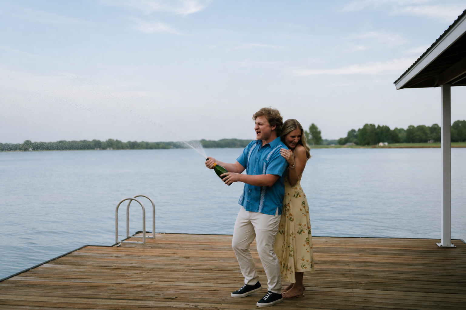 Chloe and Cal celebrating with champagne on a lakeside dock